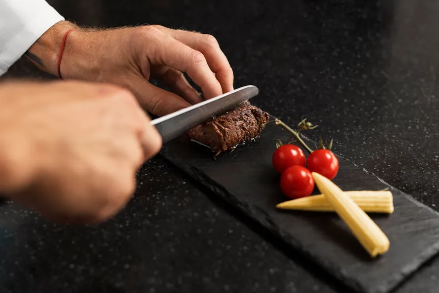 A chef slicing steak on a slate board