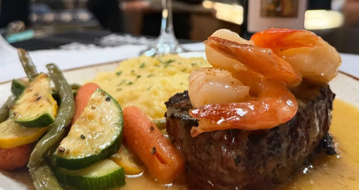 A filet topped with shrimp, with risotto and grilled vegetables